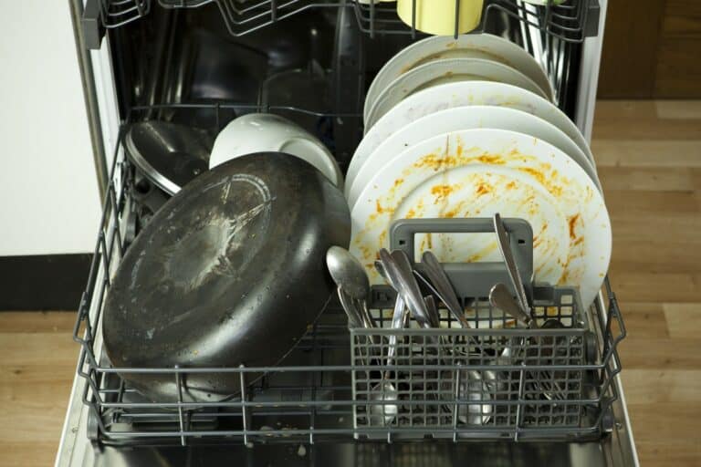 Lavavajillas mal oliente con platos y cubiertos sucios.