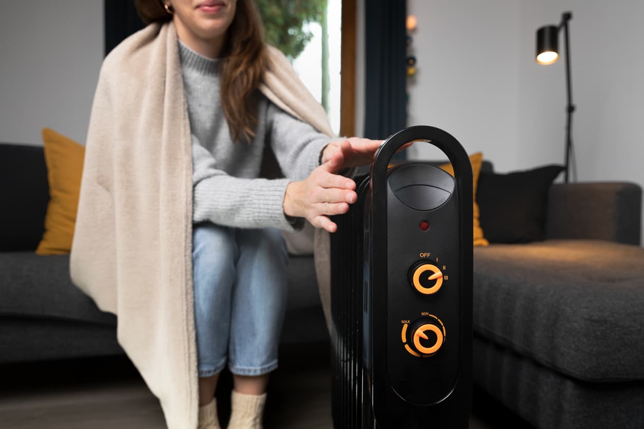 Un calefactor negro calienta las manos de una mujer en el hogar.