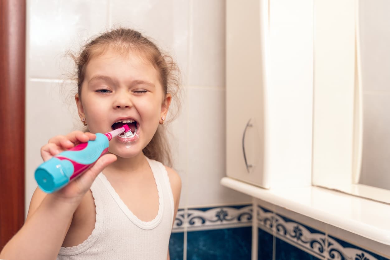Una niña se cepilla los dientes frente al espejo en el baño.