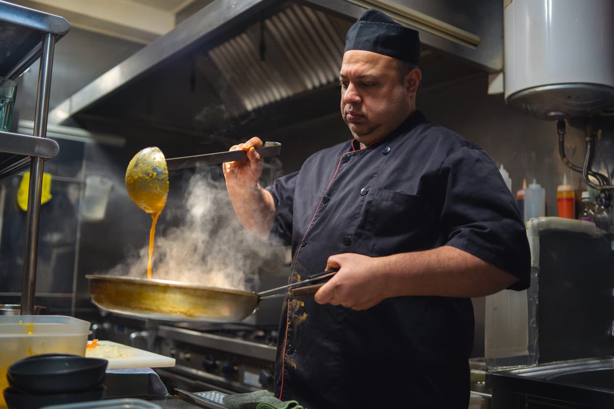 Un cocinero utiliza el cazo para remover el guiso.