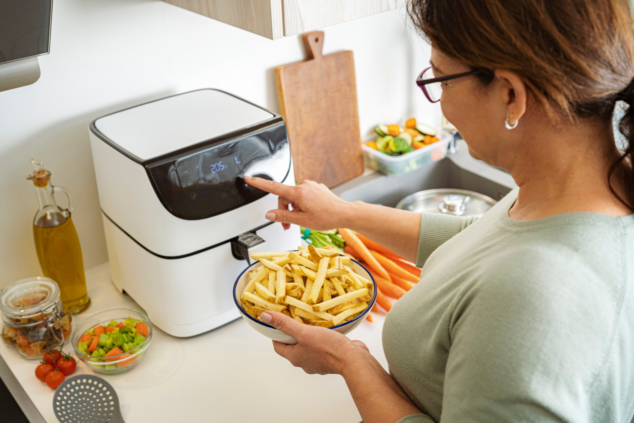 Una mujer prepara la freidora de aire para cocinar patatas fritas.