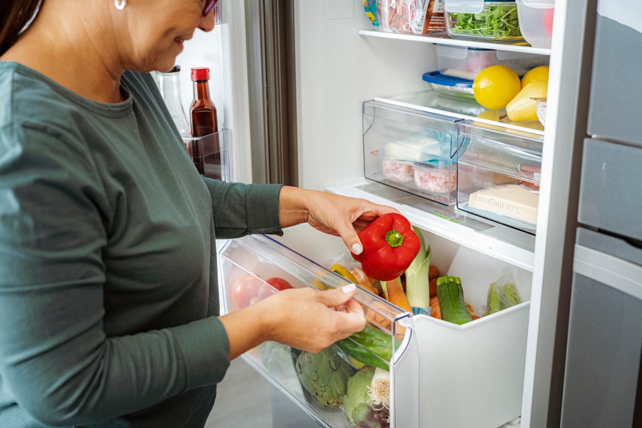Una mujer saca un pimiento del cajón de las frutas y las verduras.