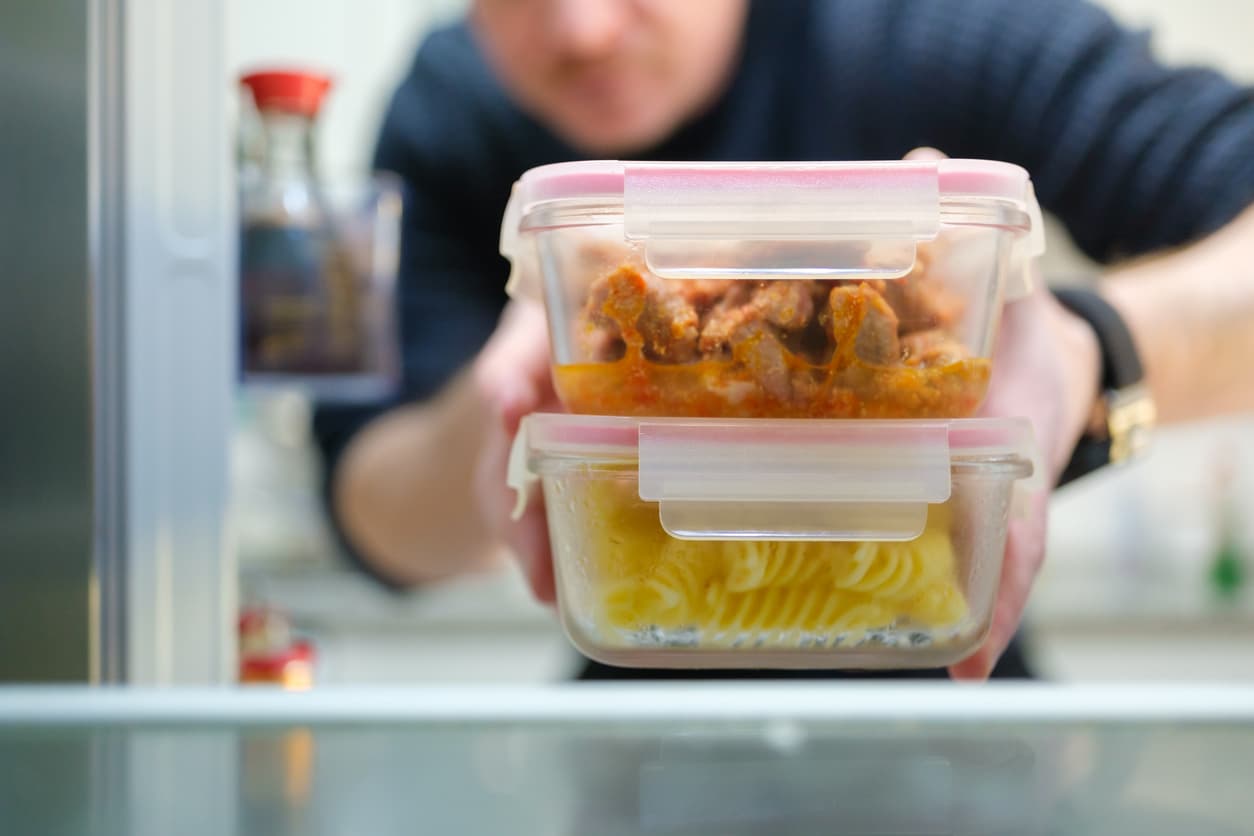 Un hombre recoge los tuppers en una balda del frigorífico.