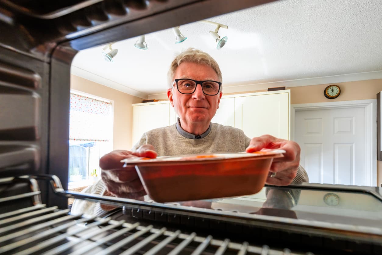 Un señor introduce un tupper en su horno-microondas con grill.