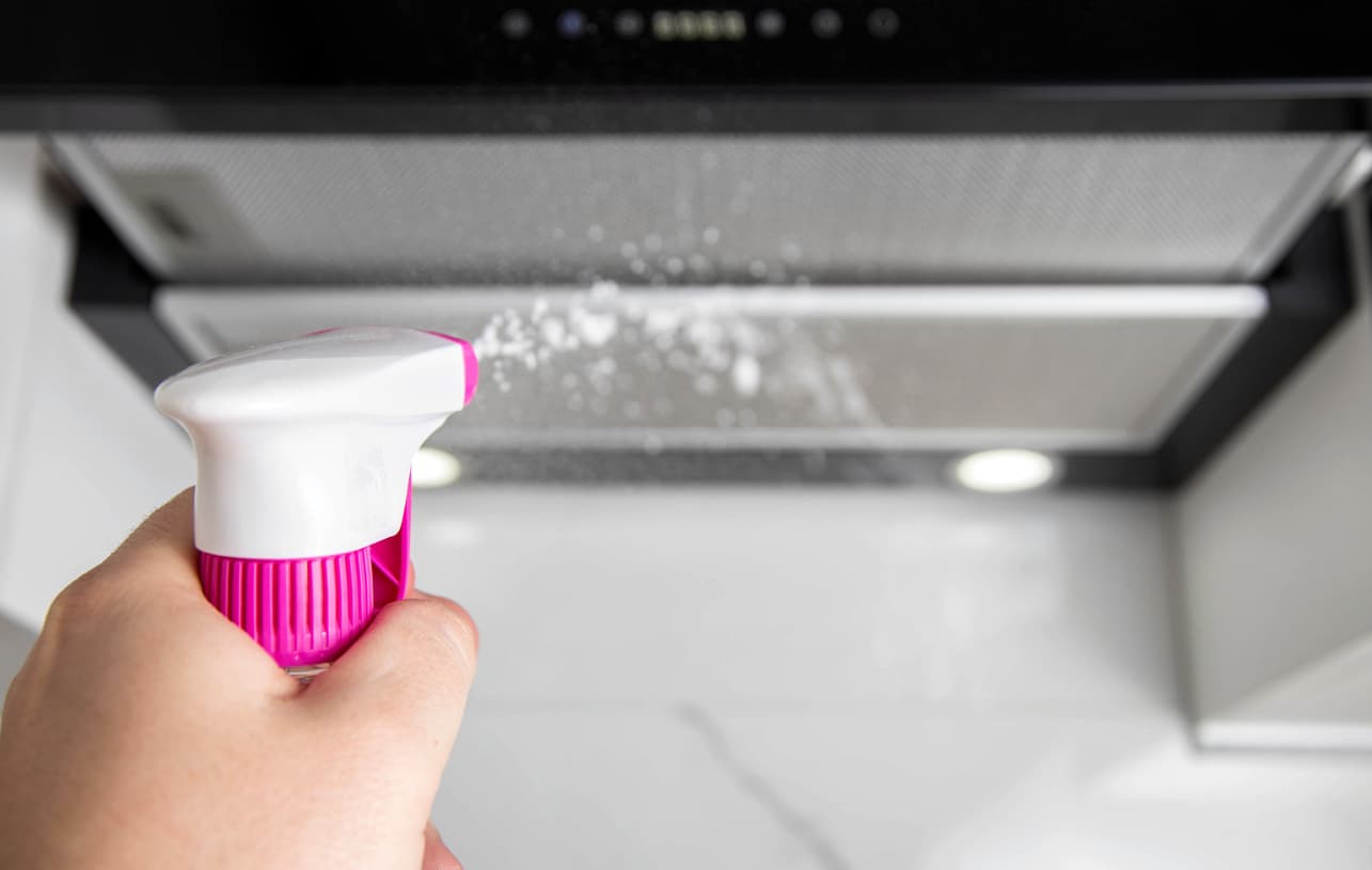 Una persona hecha un producto de limpieza para limpiar la campana  de su hogar.