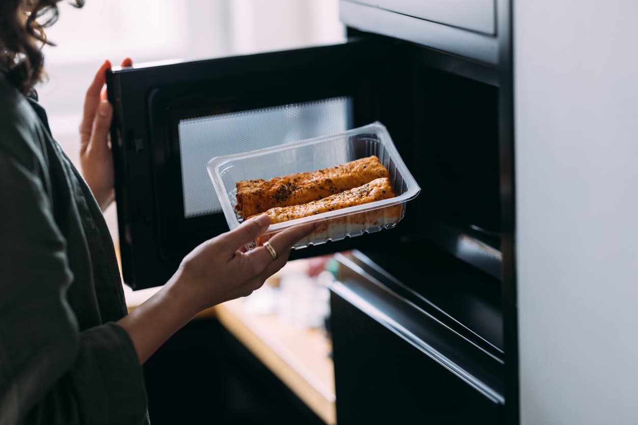 Una mujer introduce comida para calentar en el microondas.
