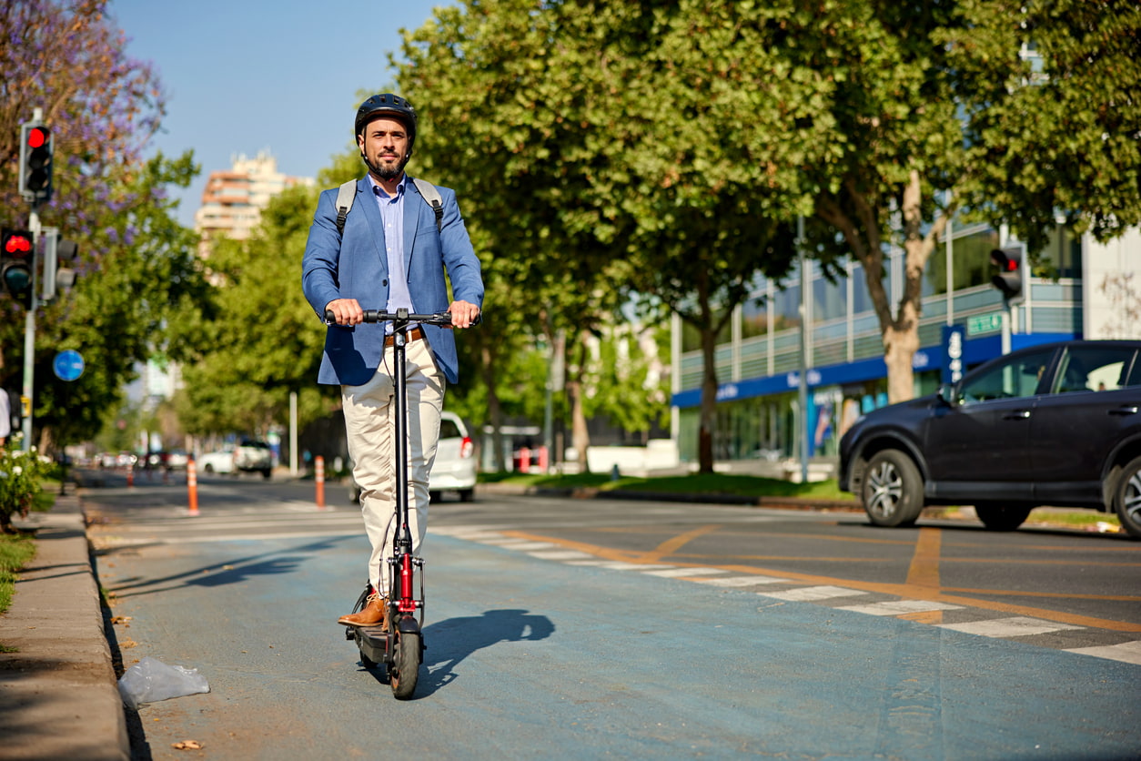 Un hombre monta en patinete eléctrico por la ciudad con casco y traje.