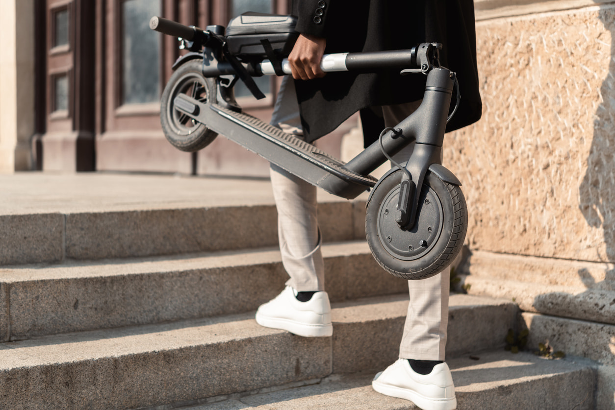 Una persona sube unas escaleras con el patinete eléctrico plegado en la mano.