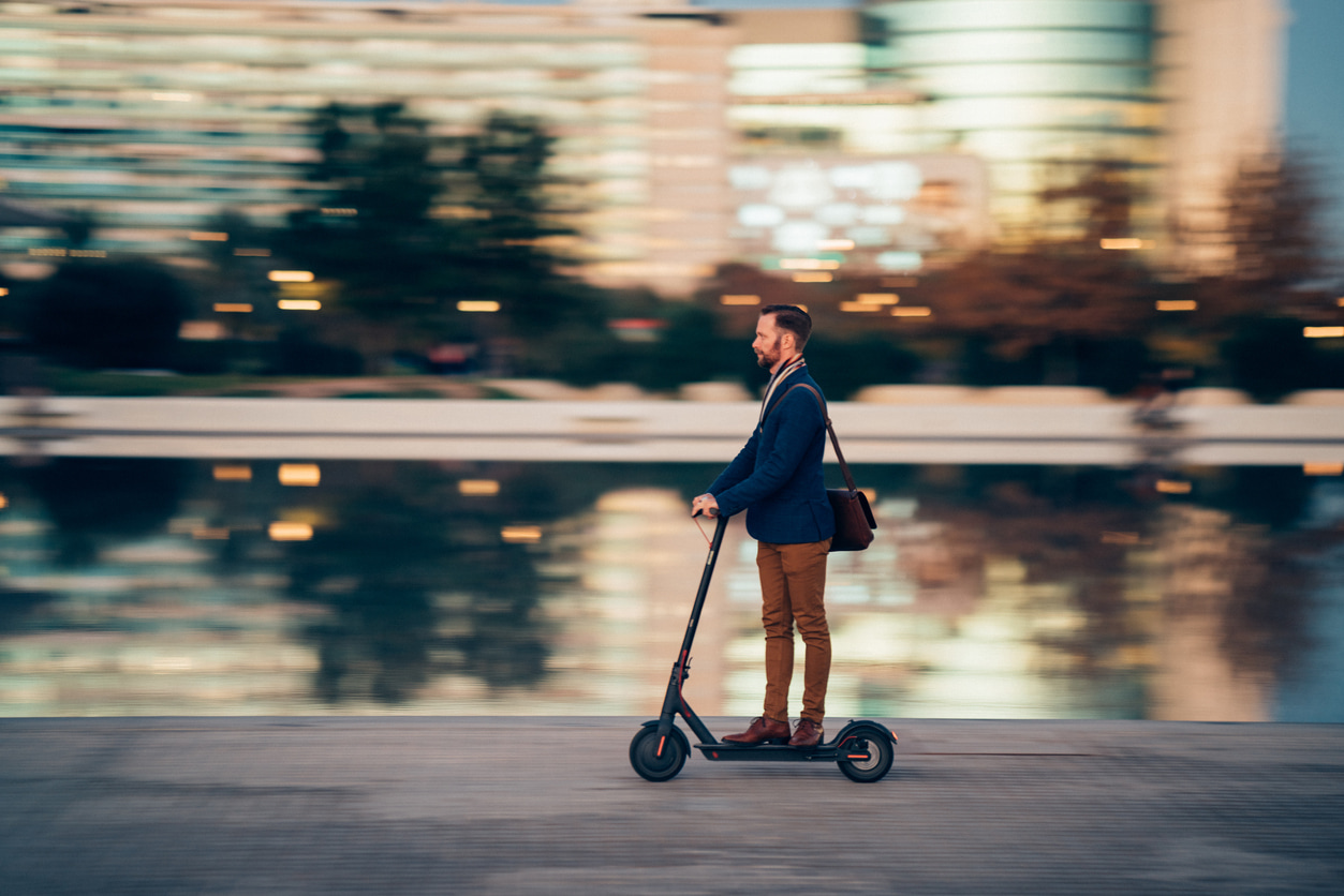 Un hombre va a trabajar con su patinete eléctrico y transporta una cartera con el ordenador.