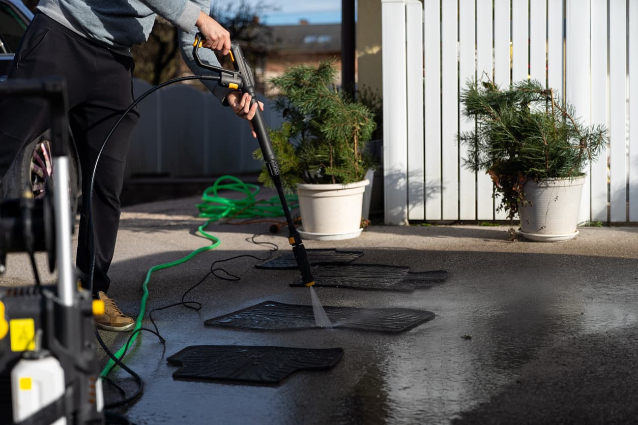Un hombre limpia alfombras con la hidrolimpiadora a presión en el jardín de su casa.