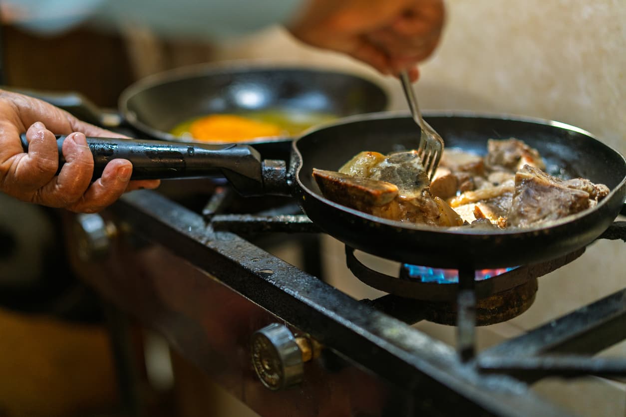 Una persona cocina carne en su placa de gas butano.