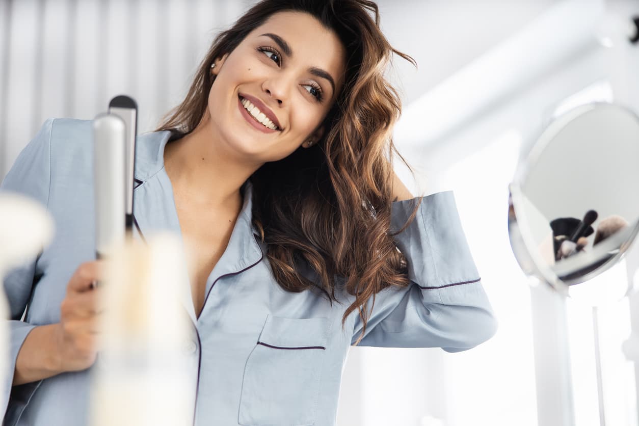 Una mujer se plancha el pelo con una plancha.