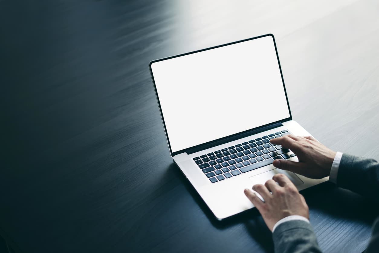 Las manos de un hombre trajeado teclean en un portátil i9 en la oficina.