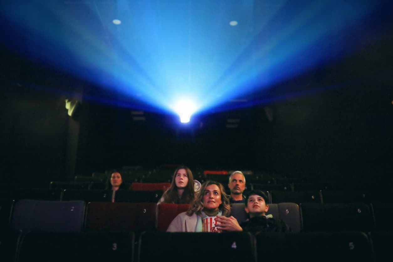 Varias personas están atentas a las imágenes del proyector de video en la sala de cine.