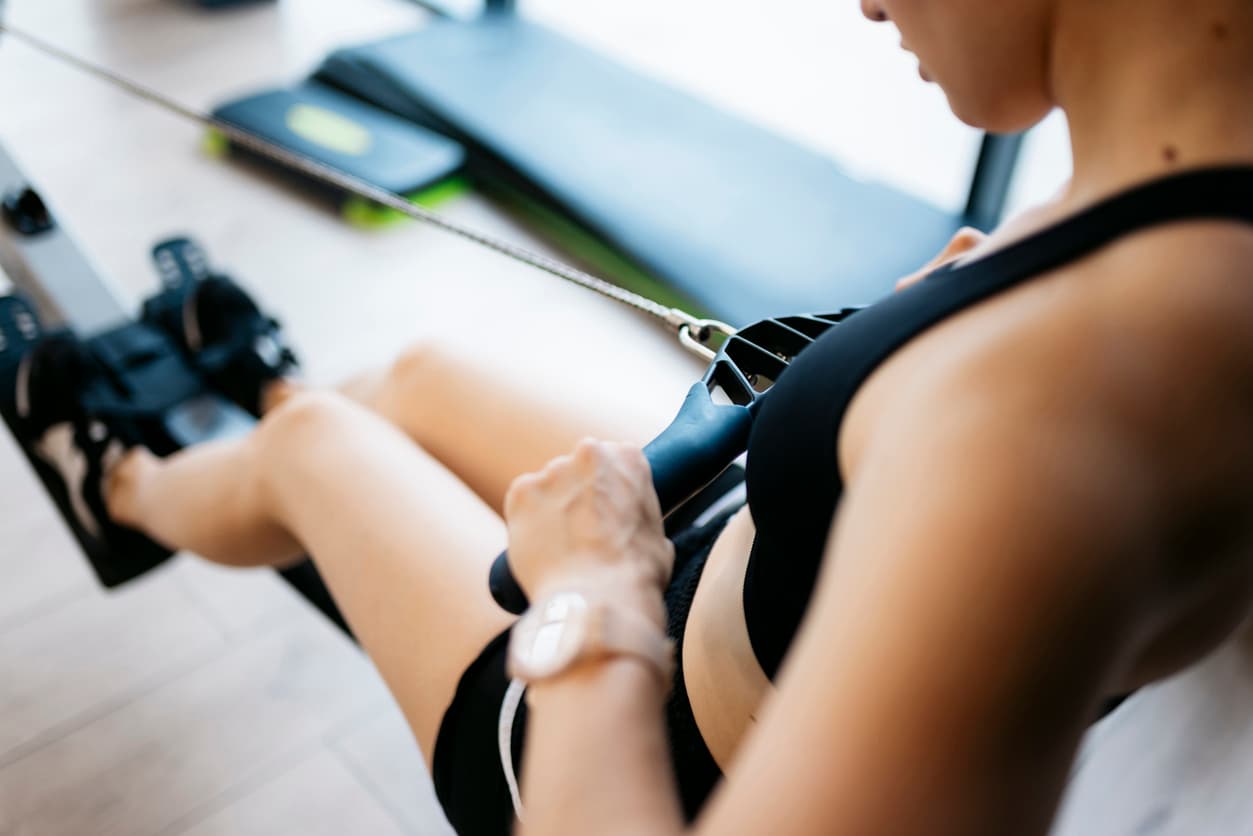 Una mujer hace deporte en la máquina de remo de su casa.