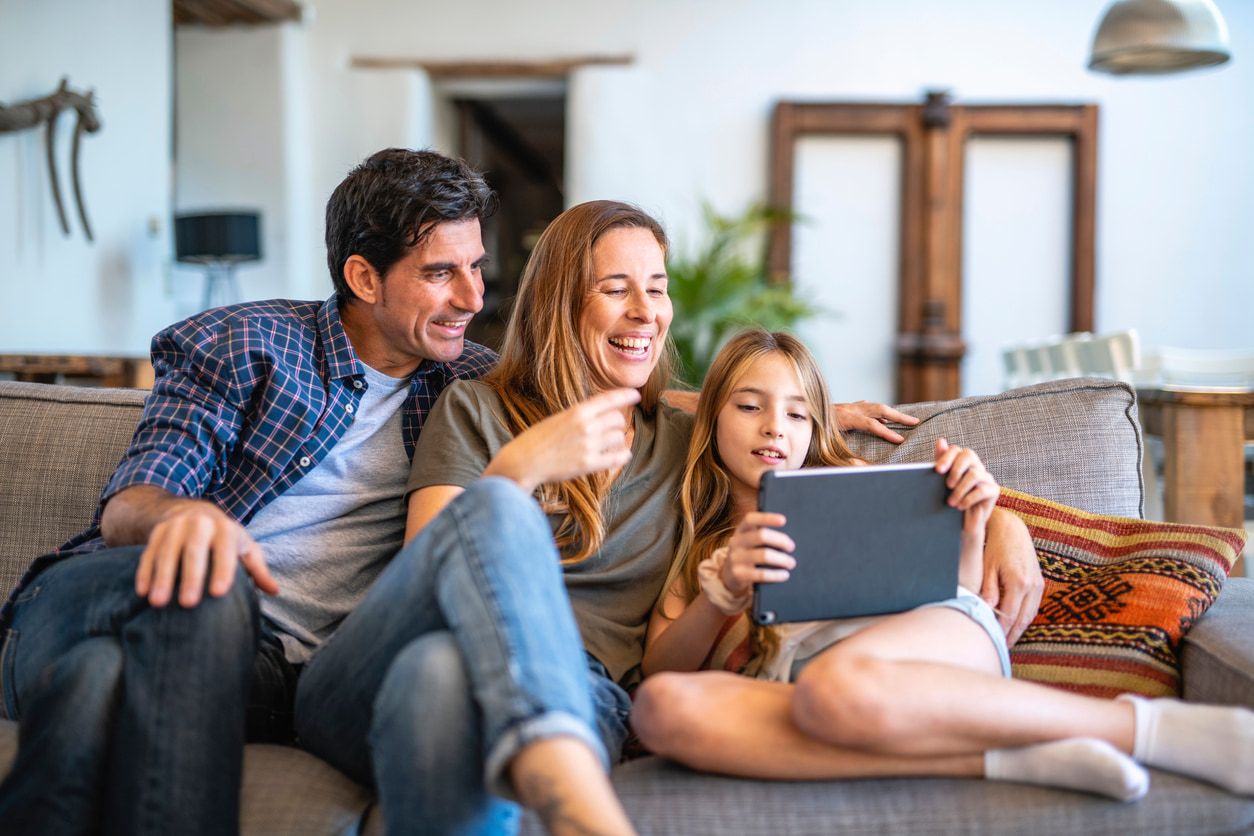 Una familia feliz comparten un contenido en la tablet Android sentados en el sofá.