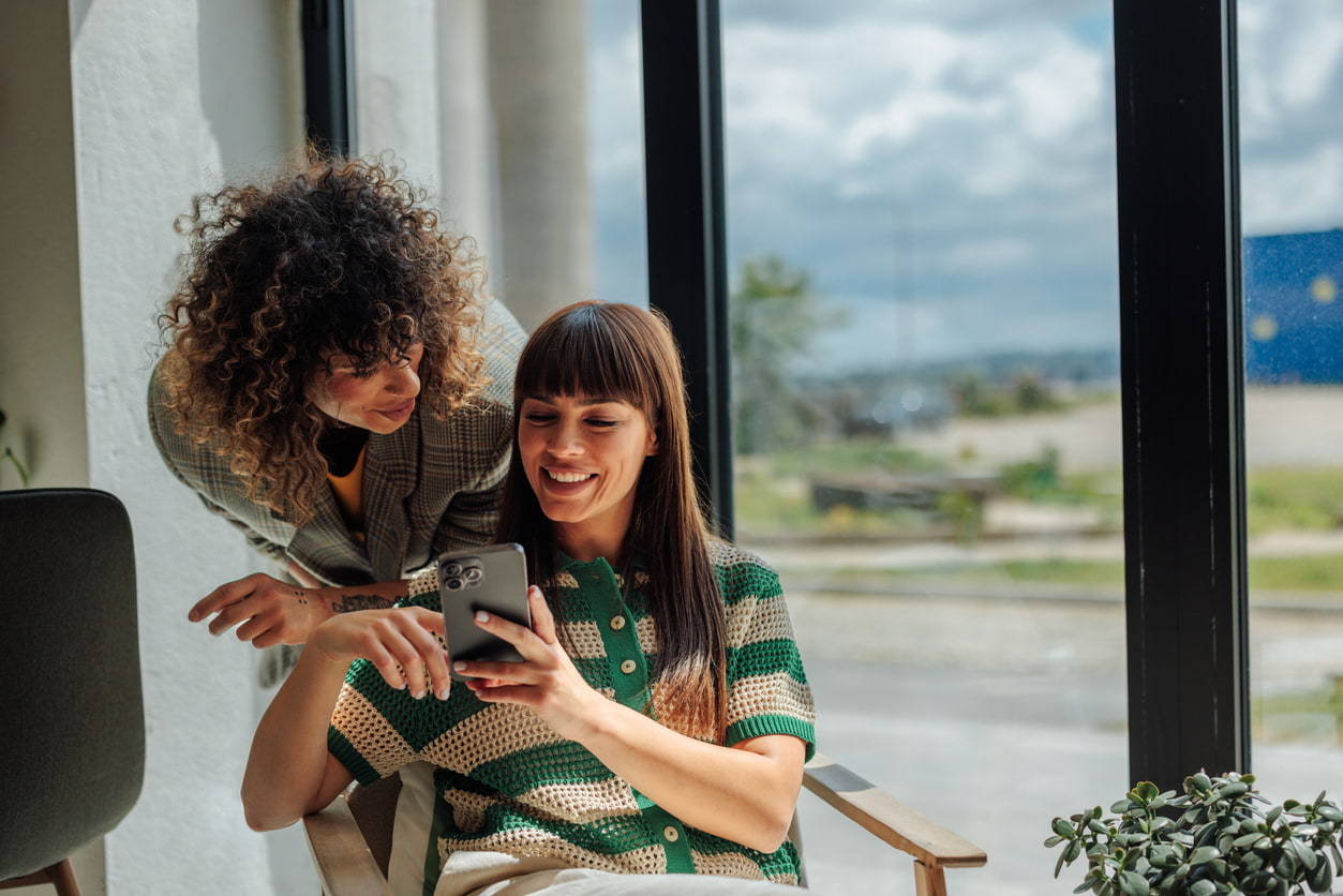 Dos chicas miran lo que aparece en el teléfono móvil y sonrien.
