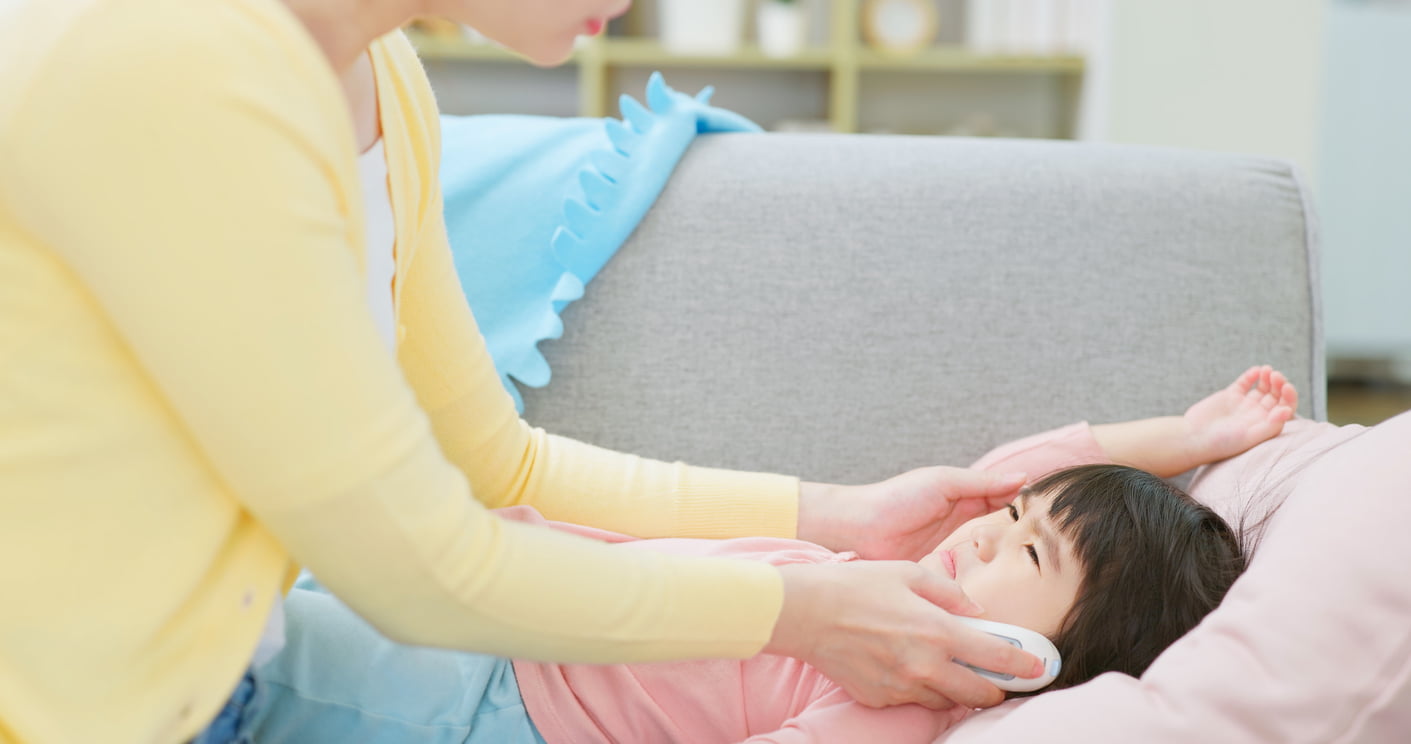 Una mujer le pone el termómetro digital de oido a su hija en la oreja.