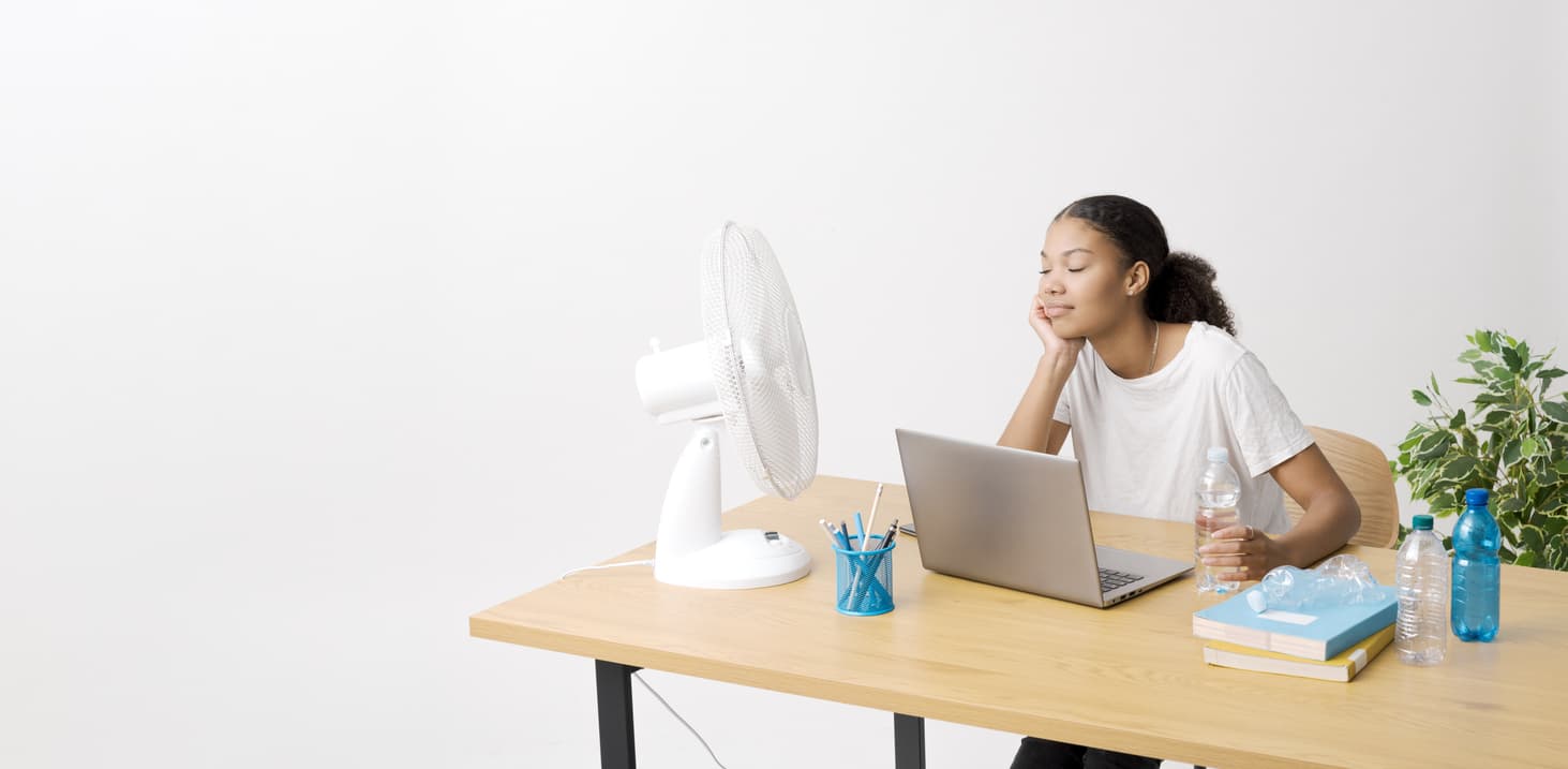 Un ventilador de mesa silencioso lo usa una mujer para concentrarse mientras estudia en su ordenador.